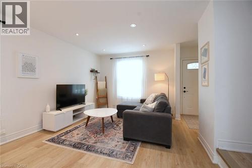 Living area featuring light wood-finish flooring, recessed lighting, a large window with sheer privacy coverings, and a white paneled entry door with frosted glass - 106 Belview Avenue, Hamilton, ON - Indoor Photo Showing Living Room