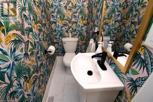 Powder room featuring botanical print wallpaper, white pedestal sink, matte black faucet, and a gold-framed mirror - 106 Belview Avenue, Hamilton, ON - Indoor Photo Showing Bathroom