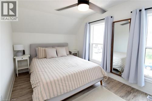 Bedroom featuring sloped ceilings, two window openings with light-colored drapes, wood-finish flooring, and a ceiling fan with integrated lighting - 106 Belview Avenue, Hamilton, ON - Indoor Photo Showing Bedroom