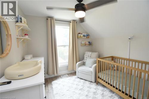 Bright room featuring sloped ceilings, a large window with drapes, wood-finish flooring, a contemporary ceiling fan with integrated lighting, and built-in shelving - 106 Belview Avenue, Hamilton, ON - Indoor Photo Showing Bedroom