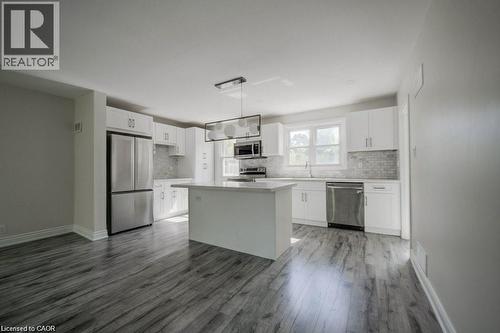 Open-concept kitchen featuring white cabinetry, stainless steel appliances, a central island, mosaic tile backsplash, and wood-finish flooring - 33 Sixth Avenue Unit# Upper, Kitchener, ON - Indoor Photo Showing Kitchen