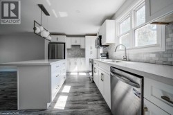 Kitchen featuring an oversized island with a white countertop, white shaker-style cabinetry with brushed nickel hardware, and wood-finish flooring - 
