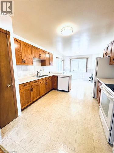 Spacious kitchen featuring wood cabinetry, white tile backsplash, and light-toned tile flooring - 42 Azores Crescent, Cambridge, ON - Indoor Photo Showing Kitchen With Double Sink