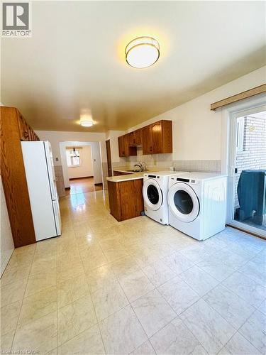 Kitchen area featuring tiled flooring, wood cabinetry, a built-in sink, and integrated laundry appliances - 42 Azores Crescent, Cambridge, ON - Indoor Photo Showing Laundry Room