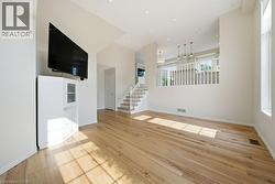Spacious living area featuring light wood-finish flooring, recessed lighting, vaulted ceilings, and a staircase with white railings - 