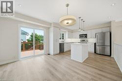 Open-concept kitchen and dining area featuring light wood-finish flooring, white cabinetry, stainless steel appliances, and a central island with a light-colored countertop - 