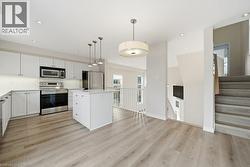 Modern kitchen featuring white cabinetry, stainless steel appliances, a center island with a stone countertop, wood-finish flooring, and recessed lighting - 