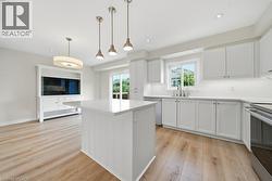 Contemporary kitchen featuring an island with a light-toned countertop, white cabinetry with silver hardware, stainless steel appliances, and wood-finish flooring - 