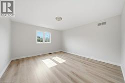 Spacious interior room featuring light wood-finish flooring, white baseboards, and a neutral wall color - 
