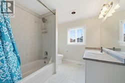 Bathroom featuring a combined tub and shower with light-toned wall tiling, a single-sink vanity with a dark countertop, a large wall-mounted mirror, and a window providing natural illumination - 