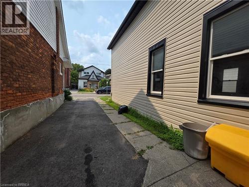 Paved driveway providing access between two structures, one featuring brick siding and the other light-colored horizontal siding with dark-trimmed windows - 109 Sydenham Street, Brantford, ON - Outdoor With Exterior