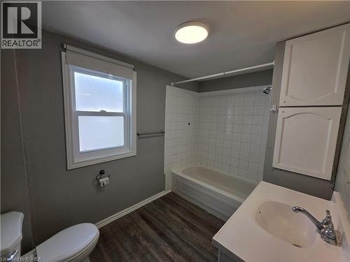 Full bathroom featuring a white single-pane window, wood-finish flooring, a combination shower and tub with white subway tile surround, a white vanity with an integrated sink, and white overhead cabin - 109 Sydenham Street, Brantford, ON - Indoor Photo Showing Bathroom