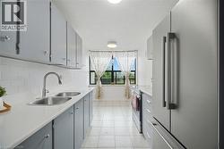 Galley kitchen featuring a double basin sink, white countertops, subway tile backsplash, and stainless steel refrigerator - 