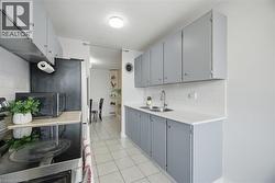 Kitchen featuring light gray cabinetry, white countertops, a double basin stainless steel sink, subway tile backsplash, and tile flooring - 
