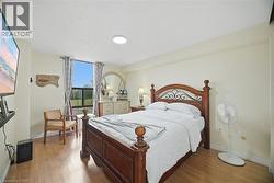 Spacious bedroom featuring wood-finish flooring, a large window with exterior landscaping visible, a ceiling-mounted light fixture, and neutral wall tones - 