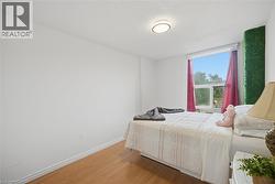 Bedroom featuring a window with natural light, wood-finish flooring, and white baseboards - 