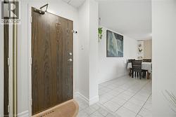 Entryway featuring a wood-look door with polished chrome hardware, white trim, and light-toned square tile flooring - 
