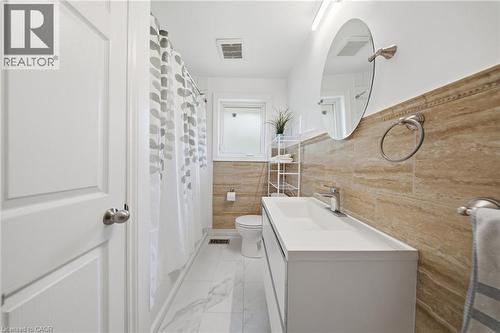 Contemporary bathroom featuring a white floating vanity with an integrated sink, brushed nickel fixtures, and a circular mirror - 80 Jackson Avenue, Kitchener, ON - Indoor