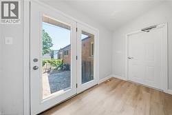 Double glass-paneled doors opening to an exterior patio with a stone-finish surface, complemented by light wood-finish flooring indoors - 