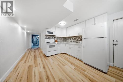 Kitchen area featuring white cabinetry, a mosaic tile backsplash, wood-finish flooring, recessed lighting, and a full suite of white appliances - 80 Jackson Avenue, Kitchener, ON - Indoor Photo Showing Kitchen