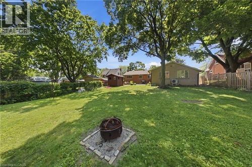 Expansive backyard featuring a large lawn area, mature trees providing natural shade, a built-in fire pit with a stone surround, a privacy fence, and a storage shed - 80 Jackson Avenue, Kitchener, ON - Outdoor