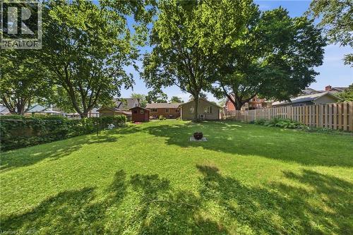Expansive backyard featuring a manicured lawn, mature trees providing natural shade, a wooden privacy fence, and a detached storage shed - 80 Jackson Avenue, Kitchener, ON - Outdoor With Backyard