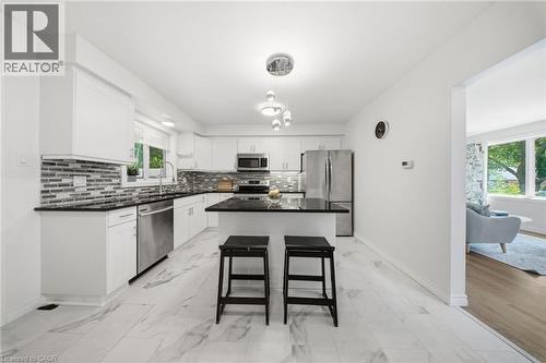 Modern kitchen featuring white cabinetry, stainless steel appliances, a center island with bar seating, a tile backsplash, and light-toned flooring - 80 Jackson Avenue, Kitchener, ON - Indoor Photo Showing Kitchen