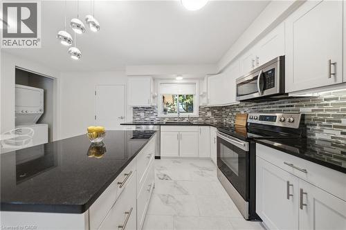 Modern kitchen featuring an expansive center island with dark countertops, white cabinetry, stainless steel appliances, a mosaic tile backsplash, and light-toned tile flooring - 80 Jackson Avenue, Kitchener, ON - Indoor Photo Showing Kitchen With Upgraded Kitchen