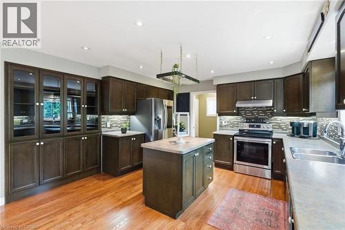 Gourmet kitchen featuring dark wood cabinetry, a central island with a light-toned countertop, stainless steel appliances, and wood-finish flooring - 5 Manor Crescent, Grimsby, ON - Indoor Photo Showing Kitchen With Double Sink With Upgraded Kitchen