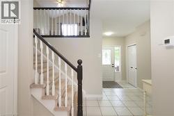 Foyer featuring a carpeted staircase with white balusters and a dark wood handrail, white tiled flooring, and a front entry door with decorative glass inserts - 