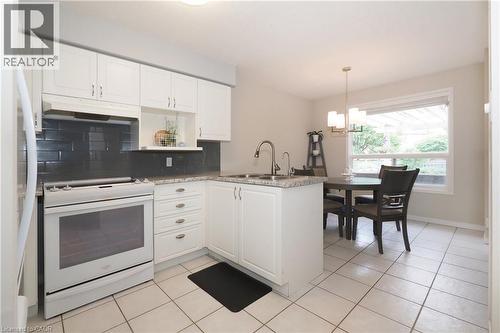 Kitchen featuring white cabinetry, dark subway tile backsplash, light-toned countertops, and tile flooring - 218 Inverhuron Crescent Unit# A, Waterloo, ON - Indoor Photo Showing Kitchen