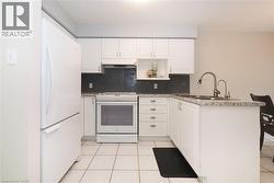 Bright kitchen featuring white cabinetry, white appliances, a dark tile backsplash, and light-toned countertops - 