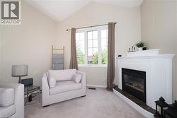 Vaulted ceiling enhancing the spaciousness of this room featuring a white mantel fireplace with a tile hearth, large multi-pane window, and light neutral wall finishes - 