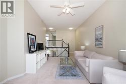 Spacious living area featuring a vaulted ceiling with a white ceiling fan, light beige walls, and soft carpet flooring - 