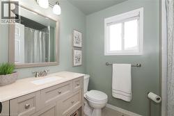 Bathroom featuring a single vanity with a neutral-toned countertop and integrated sink, brushed nickel faucet, a framed mirror, and a window with white trim - 