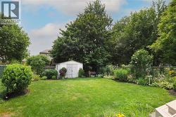 Expansive backyard featuring a manicured lawn, established garden beds, mature trees, and a functional storage shed - 