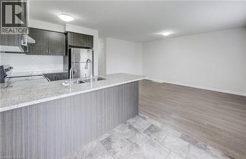 Open-concept kitchen featuring an island with a double basin sink, granite-style countertop, and wood-finish cabinetry - 823 Paris Boulevard, Waterloo, ON - Indoor Photo Showing Kitchen