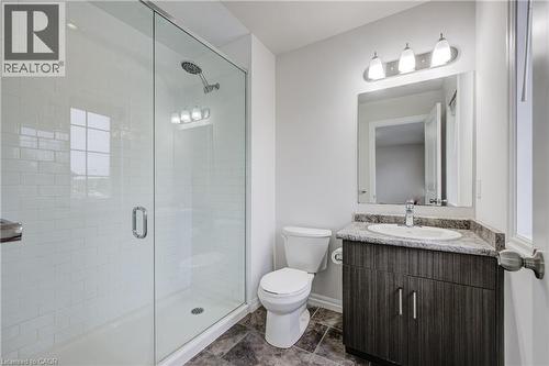 Contemporary bathroom featuring a glass-enclosed shower with white subway tile, a dark wood-finish vanity with a built-in sink and stone countertop, and a vanity mirror with a three-light fixture - 823 Paris Boulevard, Waterloo, ON - Indoor Photo Showing Bathroom