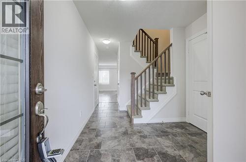 Foyer featuring slate-look tile flooring, a wood-finish entry door with clear glass panels, a staircase with wood-finish railings, and a corridor leading to additional interior spaces - 823 Paris Boulevard, Waterloo, ON - Indoor Photo Showing Other Room