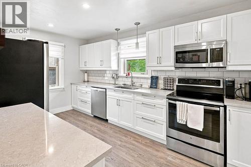 Contemporary kitchen featuring white cabinetry, stainless steel appliances, light-toned countertops, subway tile backsplash, and wood-finish flooring - 67 Weber Street S, Waterloo, ON - Indoor Photo Showing Kitchen With Stainless Steel Kitchen