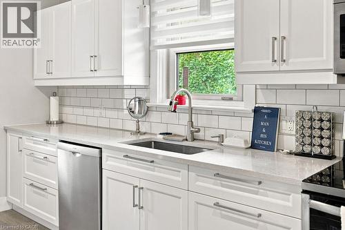 White cabinetry with stainless steel hardware, a stainless steel sink with a high-arc faucet, light-toned countertops, subway tile backsplash, and a built-in stainless steel dishwasher - 67 Weber Street S, Waterloo, ON - Indoor Photo Showing Kitchen With Upgraded Kitchen