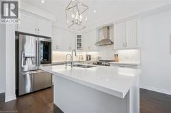 Kitchen featuring a central island with a dual-basin sink, stainless steel appliances, white shaker cabinetry, tiled backsplash, and recessed lighting - 