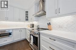 Bright kitchen featuring extensive white cabinetry, light countertops, a stainless steel range with hood, patterned backsplash, and dark wood-finish flooring - 