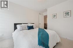 Bedroom featuring neutral wall color, light-colored carpeting, white trim, a solid panel door, and a staircase with dark wood railing visible in the background - 