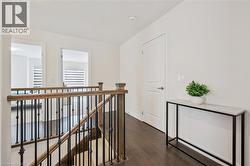 Upper landing featuring wood-finish flooring, white walls, and dark wood handrails with black metal balusters - 