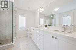 Contemporary bathroom featuring a spacious glass-enclosed shower with subway tile surround, double vanity with white cabinetry and integrated sinks, a large wall-mounted mirror, and tile flooring - 