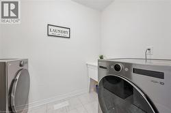 Dedicated laundry area featuring white walls, white baseboards, and light-colored tile flooring - 