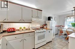 Kitchen featuring white cabinetry, grey countertops with red trim, a white tile backsplash, and a white gas range - 