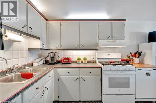 Kitchen with white cabinetry, a double basin stainless steel sink, a gas range, a white dishwasher, and dark countertops with a red trim - 98 Belwood Crescent, Kitchener, ON - Indoor Photo Showing Kitchen With Double Sink