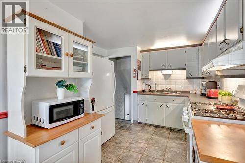 Kitchen featuring white cabinetry with dark hardware, a gas range with an overhead ventilation hood, and tile flooring - 98 Belwood Crescent, Kitchener, ON - Indoor Photo Showing Kitchen With Double Sink